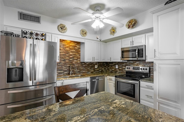 kitchen featuring appliances with stainless steel finishes, dark stone countertops, and white cabinets