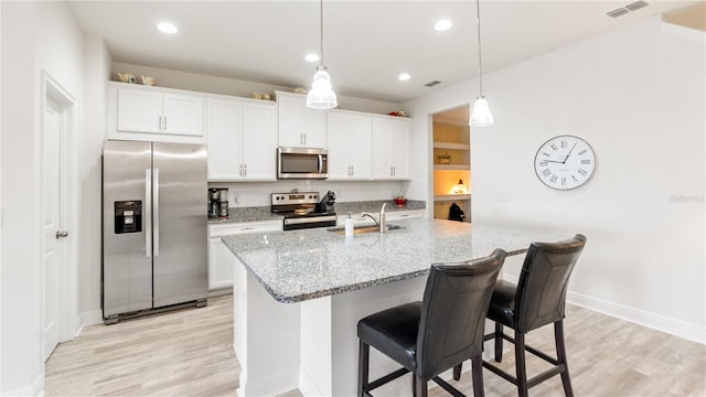 kitchen featuring appliances with stainless steel finishes, a breakfast bar, decorative light fixtures, white cabinetry, and sink