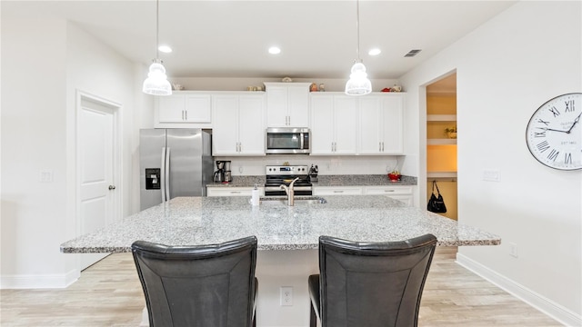 kitchen featuring white cabinetry, stainless steel appliances, a kitchen island with sink, and pendant lighting