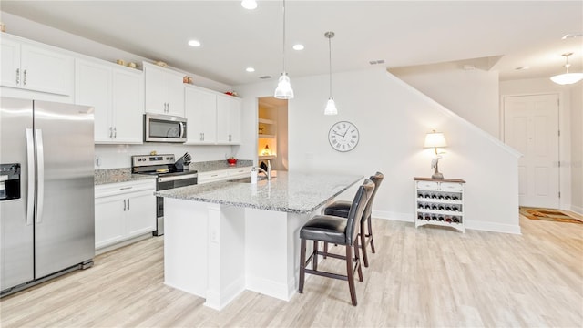 kitchen with stainless steel appliances, white cabinetry, a kitchen island with sink, and decorative light fixtures