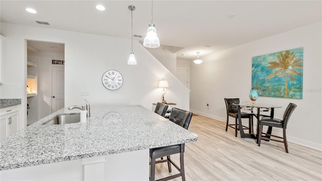 kitchen featuring a breakfast bar, sink, white cabinetry, decorative light fixtures, and light hardwood / wood-style flooring