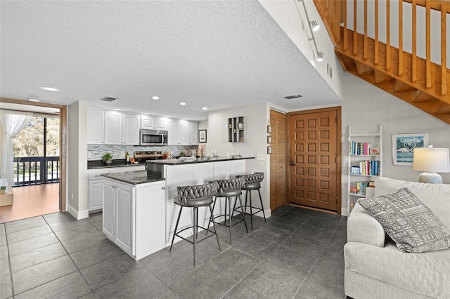 kitchen with appliances with stainless steel finishes, a kitchen breakfast bar, white cabinets, decorative backsplash, and kitchen peninsula