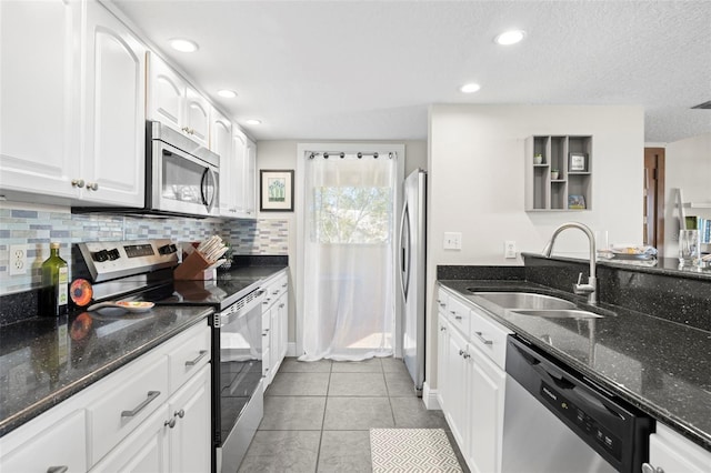 kitchen featuring appliances with stainless steel finishes, sink, dark stone countertops, white cabinets, and light tile patterned floors