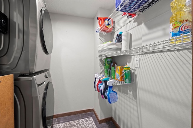 laundry room featuring dark tile patterned floors and stacked washer / drying machine