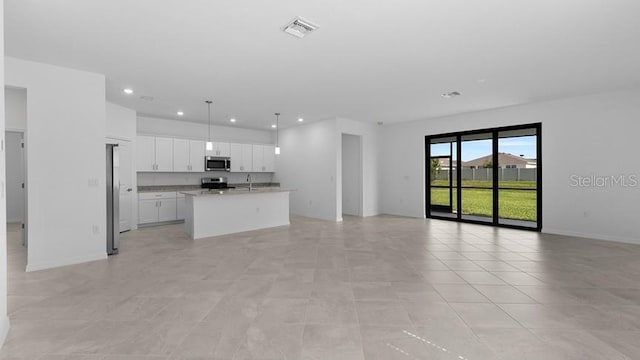 kitchen featuring white cabinetry, hanging light fixtures, a kitchen island with sink, light stone counters, and stainless steel appliances