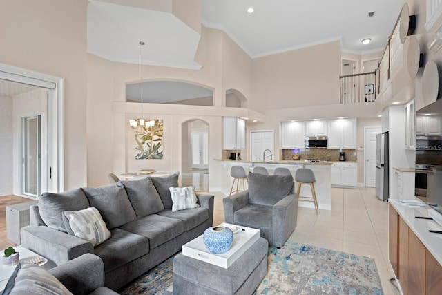 tiled living room with crown molding, a chandelier, and a high ceiling