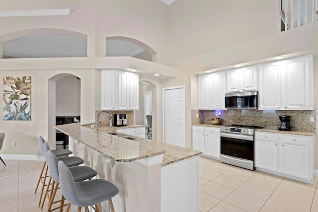 kitchen with stainless steel appliances, white cabinetry, light stone countertops, and light tile patterned floors