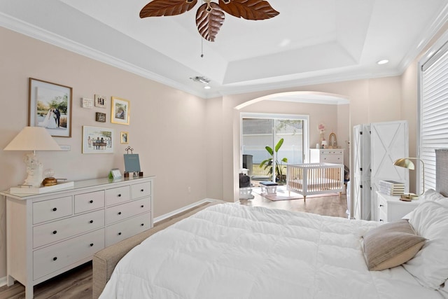 bedroom with light hardwood / wood-style flooring, ceiling fan, a tray ceiling, ornamental molding, and access to outside