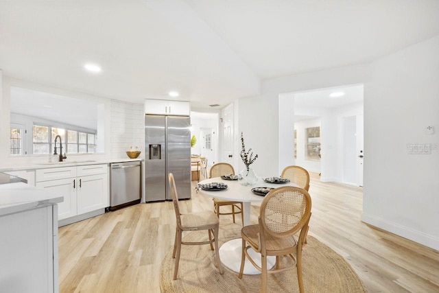 kitchen with sink, light hardwood / wood-style flooring, appliances with stainless steel finishes, white cabinetry, and decorative backsplash