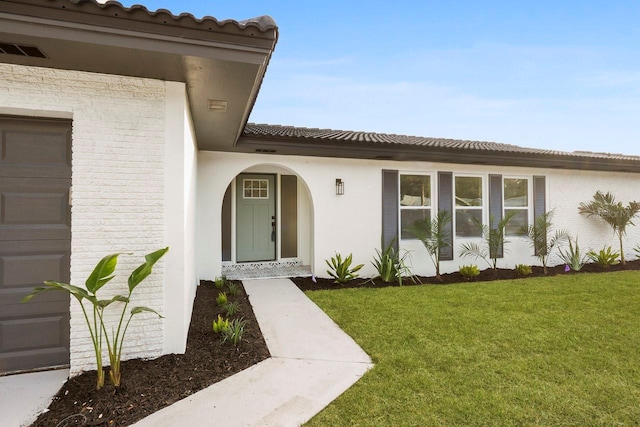 view of exterior entry featuring a garage and a lawn