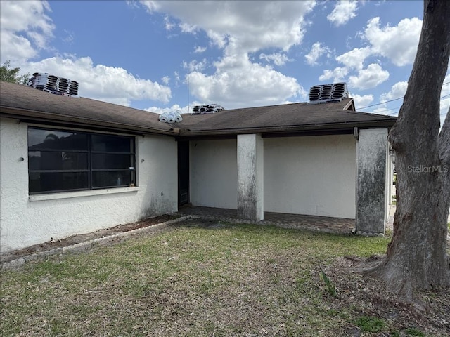 back of house with stucco siding and a lawn
