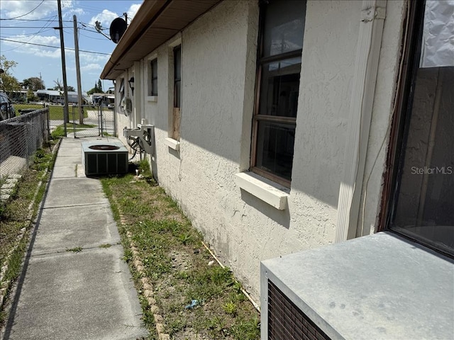 view of side of home with stucco siding, fence, and central AC