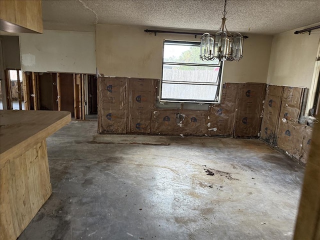 interior space with concrete floors, a textured ceiling, a chandelier, and a wainscoted wall
