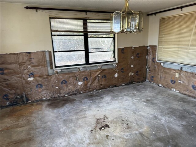 interior space with a textured ceiling, unfinished concrete floors, and a chandelier