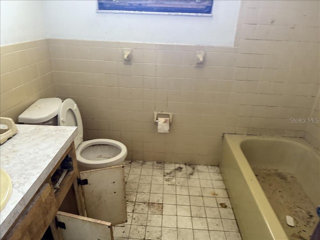 bathroom featuring a wainscoted wall, toilet, vanity, a bathtub, and tile walls