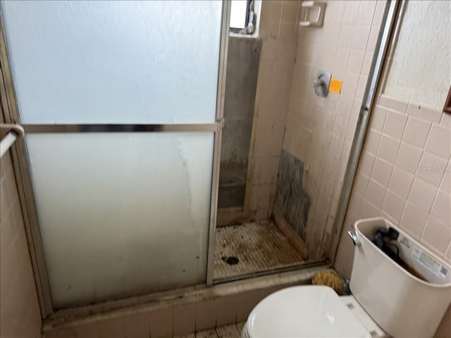 bathroom featuring toilet, tile walls, and a shower stall