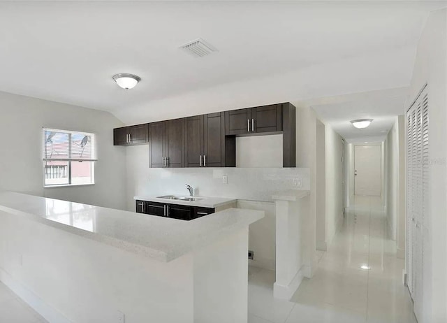 kitchen with vaulted ceiling, dark brown cabinets, sink, and light tile patterned floors