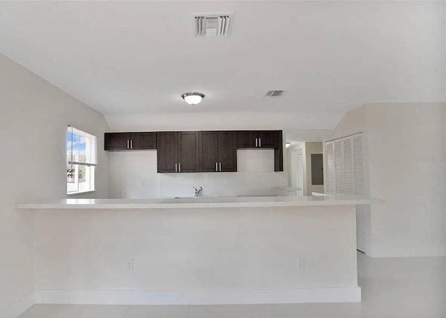 kitchen featuring vaulted ceiling, sink, dark brown cabinetry, and kitchen peninsula