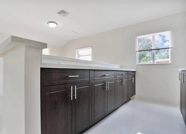 interior space featuring dark brown cabinetry, light tile patterned floors, light stone countertops, and a healthy amount of sunlight