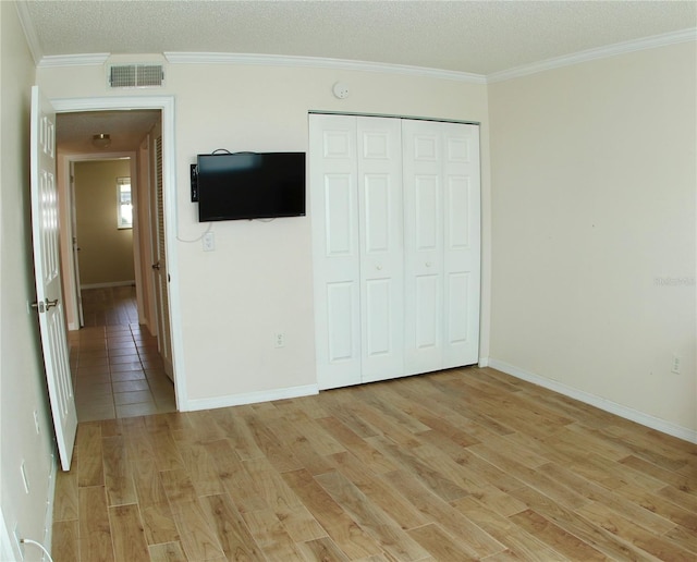 unfurnished bedroom with crown molding, a textured ceiling, a closet, and light wood-type flooring