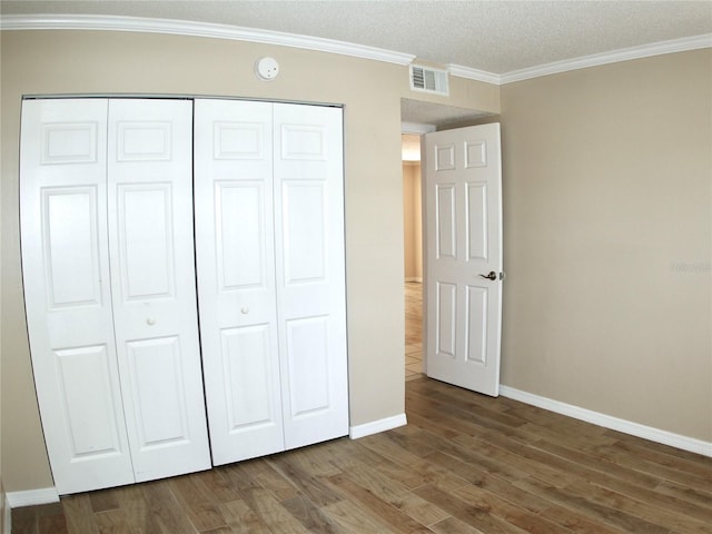 unfurnished bedroom with dark wood-type flooring, ornamental molding, and a closet