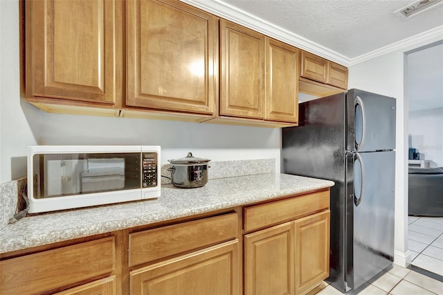 kitchen featuring black refrigerator, ornamental molding, a textured ceiling, and light tile patterned floors