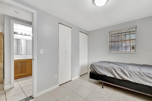 bedroom with two closets, sink, a textured ceiling, and light tile patterned floors