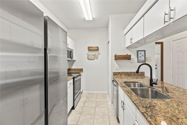 kitchen with sink, light tile patterned floors, appliances with stainless steel finishes, white cabinetry, and dark stone counters