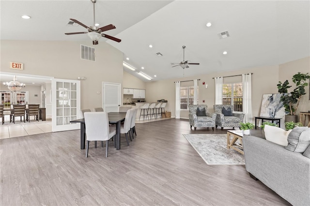 living room featuring ceiling fan with notable chandelier, high vaulted ceiling, and light hardwood / wood-style flooring