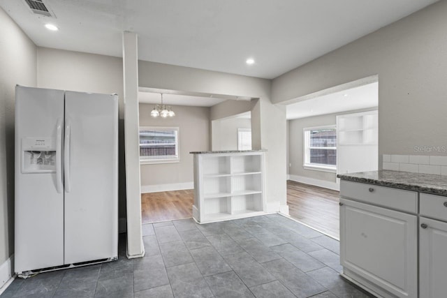 kitchen featuring white cabinetry, white refrigerator with ice dispenser, a chandelier, and pendant lighting