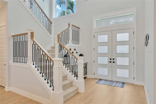 foyer entrance with french doors, light hardwood / wood-style floors, and a high ceiling