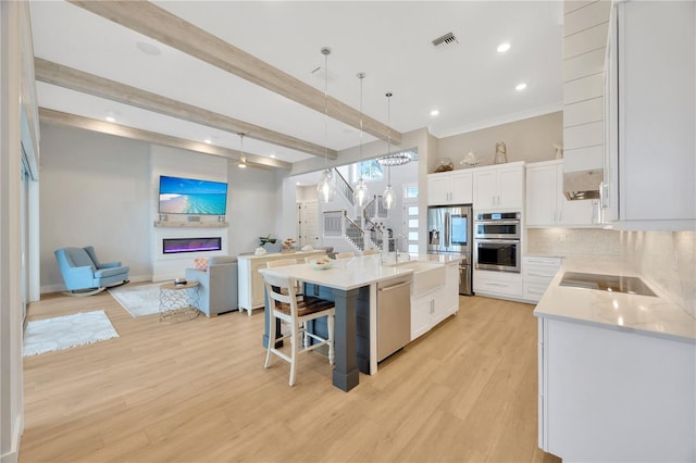 kitchen with hanging light fixtures, appliances with stainless steel finishes, a kitchen breakfast bar, a kitchen island with sink, and white cabinets