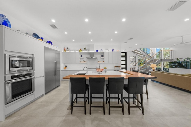 kitchen with a large island, sink, white cabinetry, a kitchen breakfast bar, and built in appliances