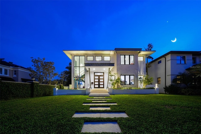 back of house at night with stucco siding, a lawn, and french doors