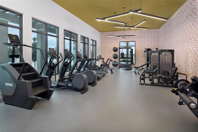 exercise room with wallpapered walls and a towering ceiling