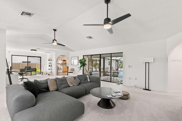 living room featuring a textured ceiling, vaulted ceiling, light colored carpet, and ceiling fan