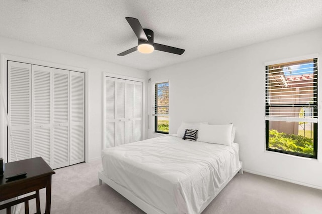 bedroom featuring light carpet, ceiling fan, a textured ceiling, and multiple closets