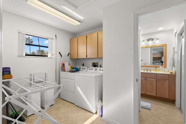 laundry room with sink, cabinets, light tile patterned floors, washing machine and clothes dryer, and a textured ceiling