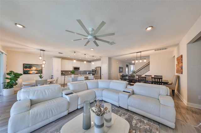 living room with ceiling fan with notable chandelier, a textured ceiling, and light hardwood / wood-style floors