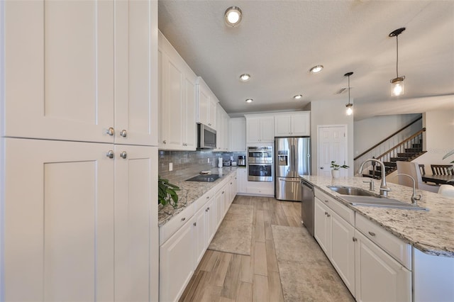 kitchen with sink, decorative light fixtures, a center island with sink, stainless steel appliances, and white cabinets