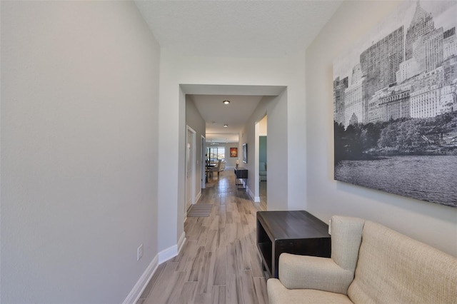 hallway featuring light wood-style flooring, baseboards, and a textured ceiling