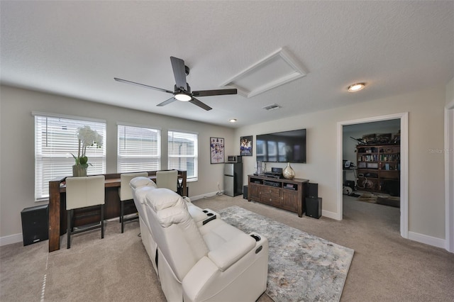 living area featuring a textured ceiling, light colored carpet, visible vents, baseboards, and attic access