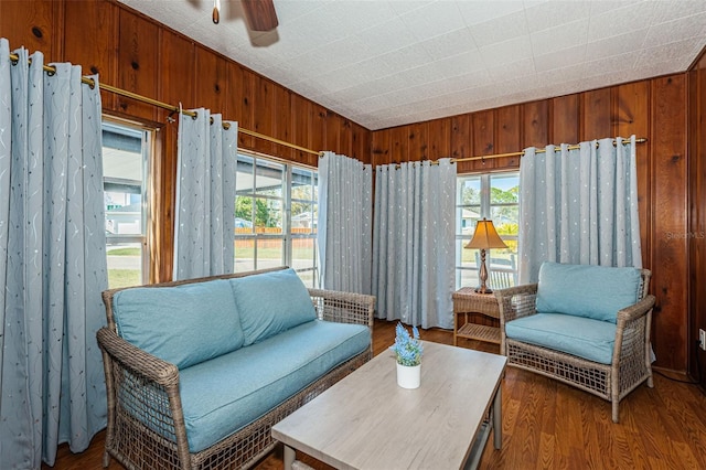 living room featuring dark wood-type flooring, ceiling fan, and wood walls