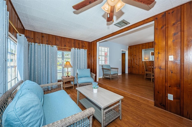 living room with wood-type flooring, wooden walls, and ceiling fan