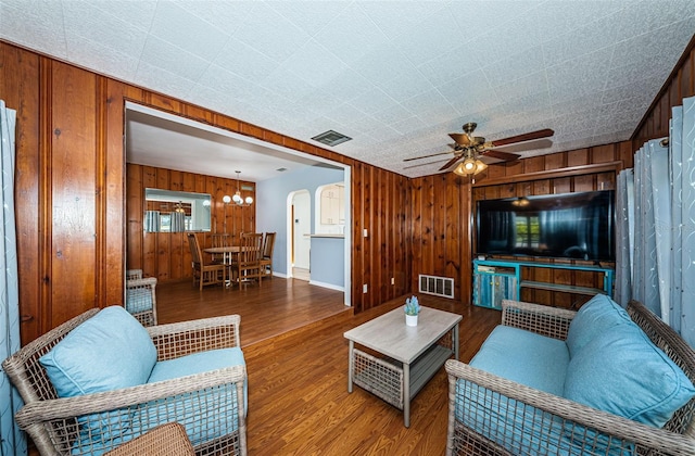 living room with hardwood / wood-style flooring, ceiling fan with notable chandelier, and wooden walls