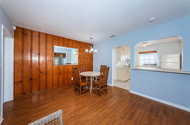 dining room with ceiling fan with notable chandelier, light hardwood / wood-style floors, sink, and wood walls