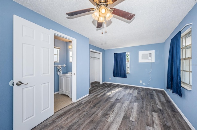 unfurnished bedroom with dark wood-type flooring, a wall mounted AC, a textured ceiling, a closet, and ceiling fan