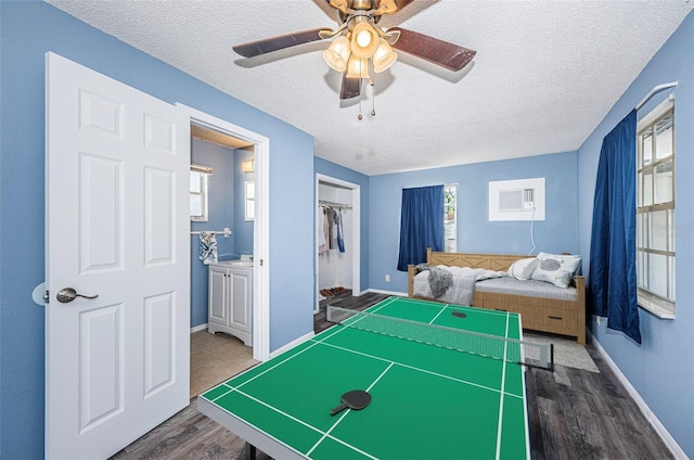 recreation room featuring dark wood-type flooring, a wall unit AC, and a textured ceiling