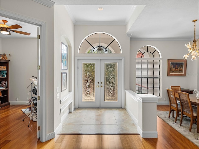 foyer with ornamental molding, light hardwood / wood-style flooring, an inviting chandelier, and french doors