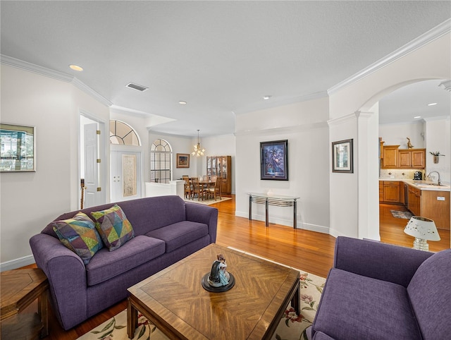 living room featuring an inviting chandelier, ornamental molding, sink, and light hardwood / wood-style floors